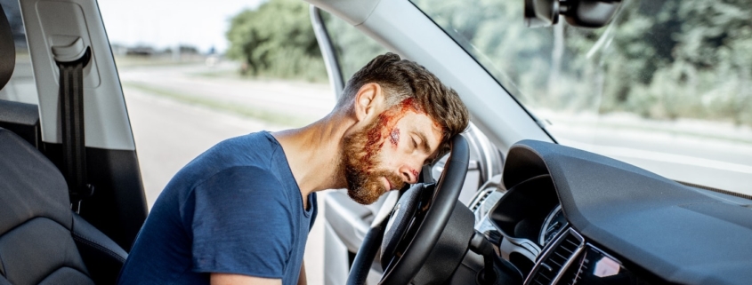 Bodily injury resulting from car accident.. Bloodied man unconscious in drivers seat with with head resting on steering wheel.