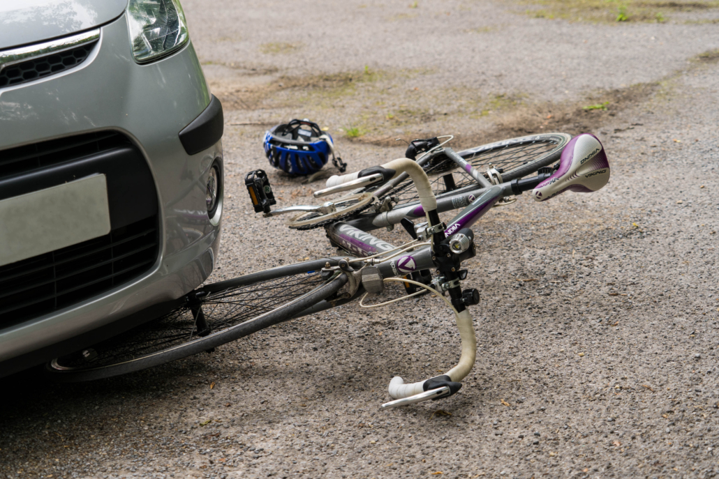 A bike lies partially crushed beneath a car following a traffic collision