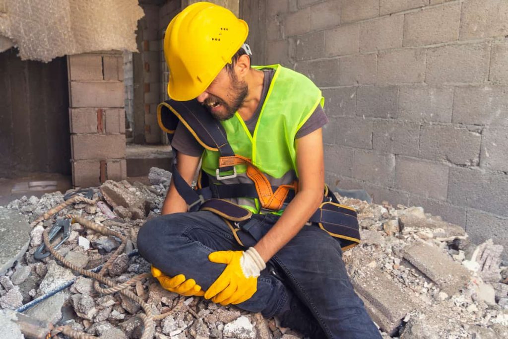 A construction worker holds his leg after injuring it in a workplace accident. Luckily, his injury is covered by workers comp.