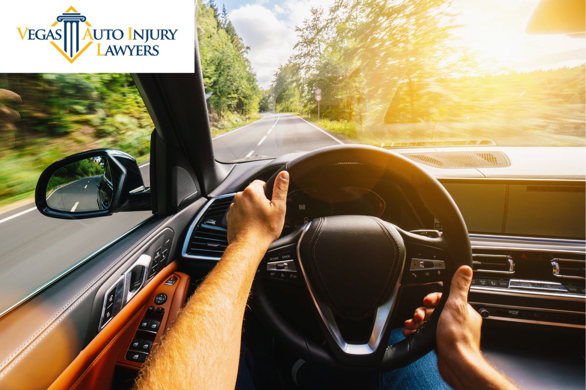 Vegas Auto Injury Lawyers explains Coping with Physical and Emotional Trauma After A Car Accident with a photo of a first-person view of hands on a steering wheel inside the interior of a car headed towards a sun-lit road.